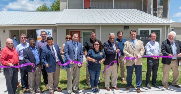 Public Officials standing with scissors cutting a ribbon in front of Fox Run Clubhouse