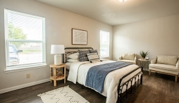 master bedroom with bed, nighstand, two armchairs, rug, two windows
