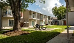 Two-story apartment building with balconies and picnic table near shade tree